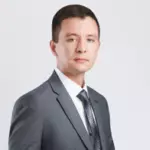 Чоловік у сірому костюмі, білій сорочці та краватці з візерунком стоїть на однотонному світлому тлі, дивлячись уперед з нейтральним виразом обличчя. ГО Український Альянс